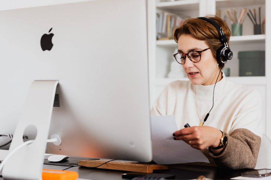 A woman sits at home recording audio on her headphone's microphone